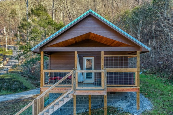 Covered deck with metal railing overlooking forested property with brick house visible in distance
